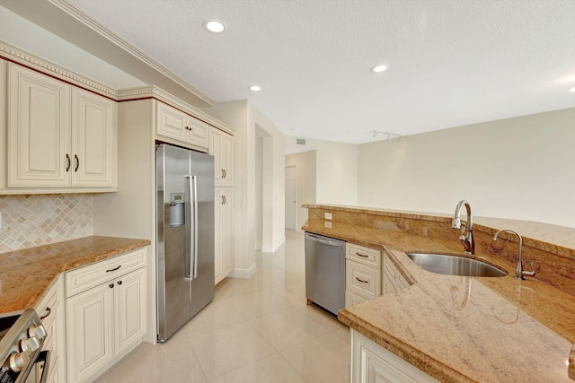 kitchen with stainless steel appliances, sink, cream cabinets, tasteful backsplash, and light stone countertops