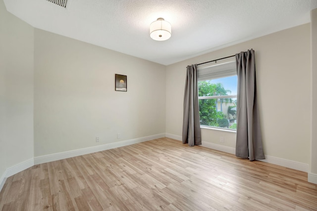 empty room with light wood-type flooring and a textured ceiling