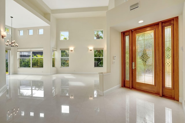 tiled foyer entrance featuring a high ceiling, plenty of natural light, and an inviting chandelier