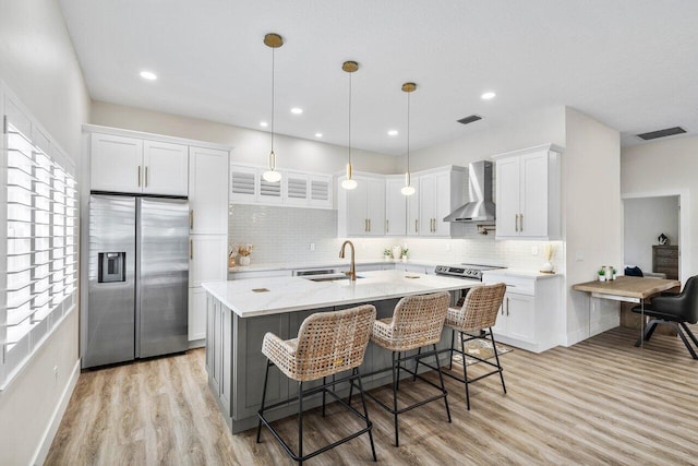 kitchen with sink, stainless steel refrigerator with ice dispenser, wall chimney exhaust hood, decorative light fixtures, and white cabinets