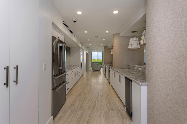 kitchen with light stone countertops, decorative light fixtures, stainless steel fridge, and white cabinets