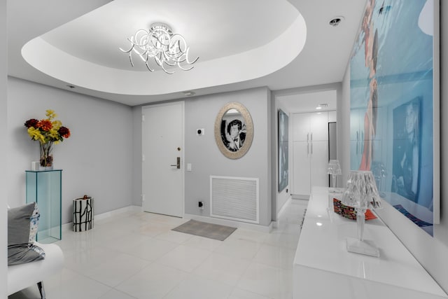 tiled entryway featuring a tray ceiling and an inviting chandelier