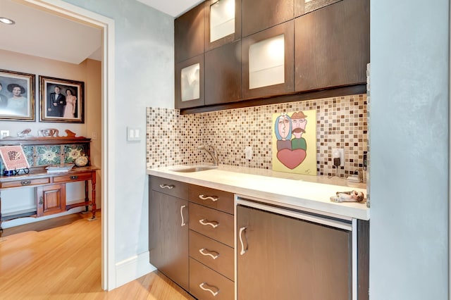 kitchen featuring dark brown cabinets, light hardwood / wood-style flooring, backsplash, and sink