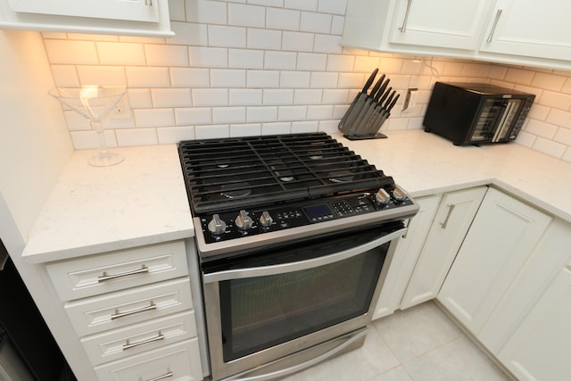 kitchen featuring light stone counters, white cabinets, light tile patterned floors, tasteful backsplash, and stainless steel gas range