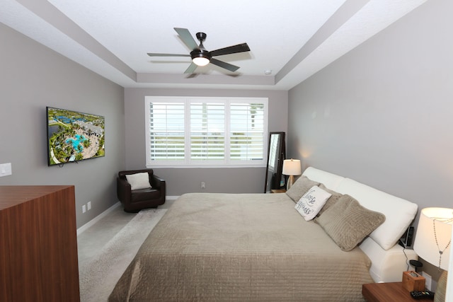 carpeted bedroom with a tray ceiling and ceiling fan