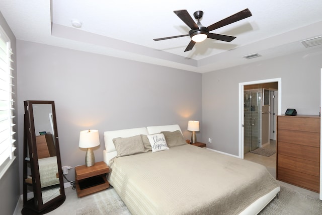 bedroom with light carpet, ceiling fan, a tray ceiling, and connected bathroom