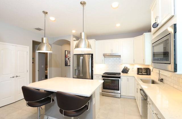 kitchen featuring white cabinetry, sink, appliances with stainless steel finishes, decorative light fixtures, and a kitchen island