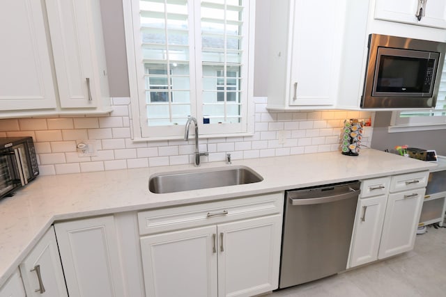 kitchen with stainless steel appliances, white cabinets, sink, and light stone counters