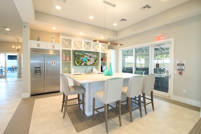 kitchen with a spacious island, stainless steel built in refrigerator, a breakfast bar, white cabinetry, and decorative light fixtures