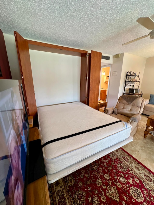 bedroom featuring ceiling fan, light tile patterned floors, and a textured ceiling