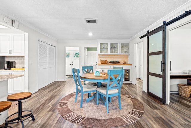 dining area with a textured ceiling, dark wood-type flooring, a barn door, and crown molding