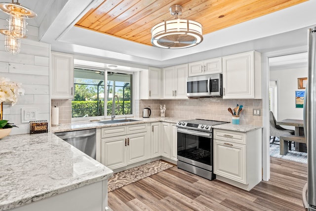 kitchen with stainless steel appliances, white cabinetry, decorative light fixtures, light stone countertops, and light hardwood / wood-style flooring