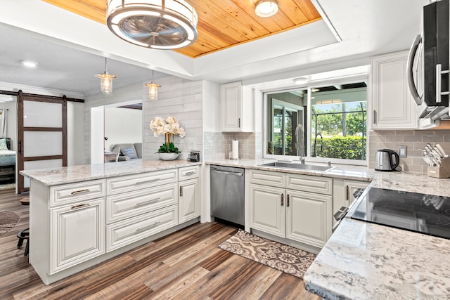 kitchen with stainless steel appliances, a barn door, sink, white cabinets, and kitchen peninsula