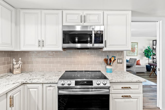 kitchen with white cabinets, hardwood / wood-style flooring, backsplash, light stone countertops, and appliances with stainless steel finishes