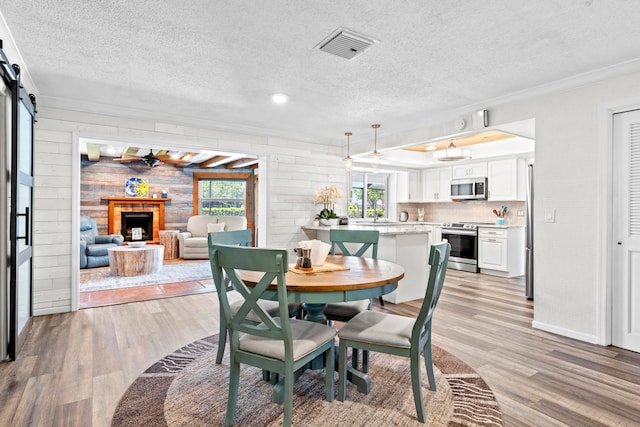 dining area with a barn door, wooden walls, ornamental molding, ceiling fan, and light wood-type flooring