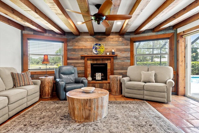 living room featuring ceiling fan, beamed ceiling, a healthy amount of sunlight, and a tile fireplace