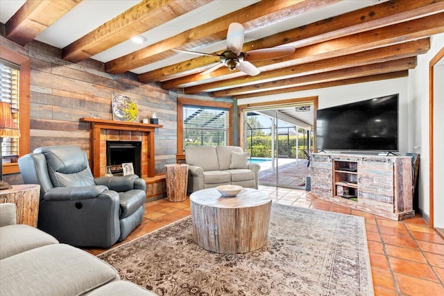 tiled living room featuring a tiled fireplace, wooden walls, ceiling fan, and beam ceiling