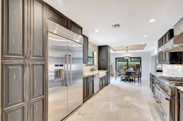 kitchen with light stone countertops, hanging light fixtures, backsplash, high quality appliances, and dark brown cabinets