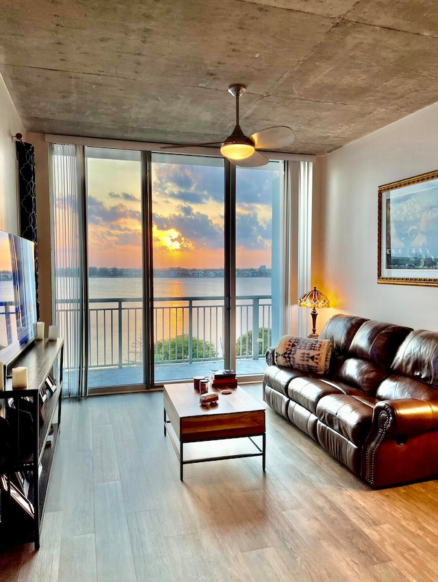 living room featuring hardwood / wood-style floors, a water view, floor to ceiling windows, and ceiling fan