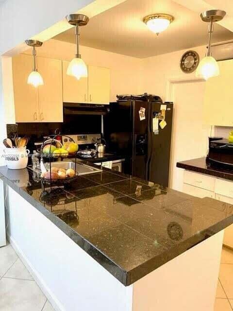 kitchen with black refrigerator with ice dispenser, decorative light fixtures, light tile patterned floors, sink, and kitchen peninsula