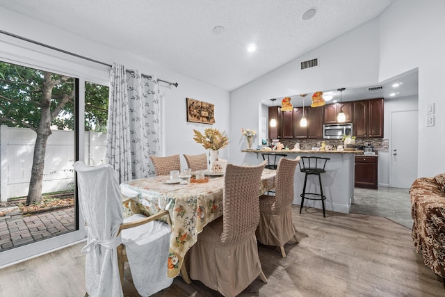 dining area featuring light hardwood / wood-style floors, a textured ceiling, and high vaulted ceiling