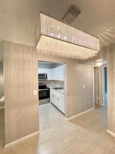 kitchen with stainless steel appliances, decorative backsplash, sink, white cabinetry, and light wood-type flooring