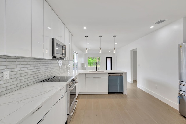 kitchen featuring stainless steel appliances, pendant lighting, kitchen peninsula, sink, and white cabinetry