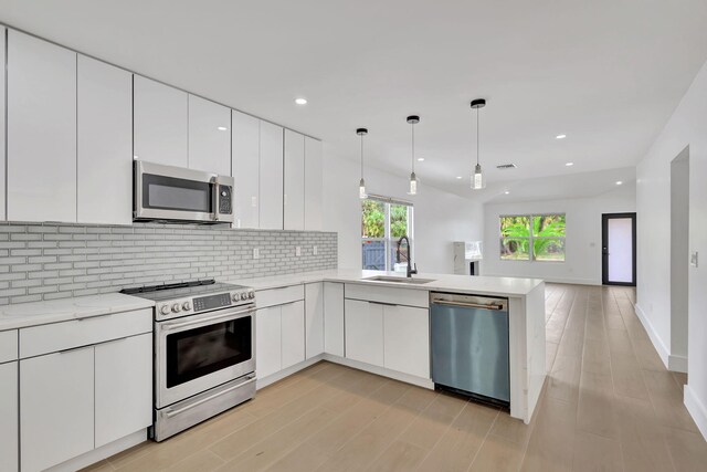 kitchen with sink, appliances with stainless steel finishes, decorative light fixtures, light hardwood / wood-style flooring, and white cabinets