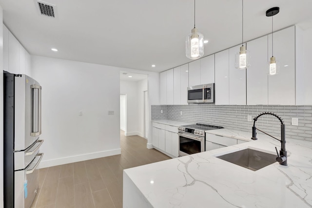 kitchen featuring light stone counters, stainless steel appliances, pendant lighting, sink, and white cabinets