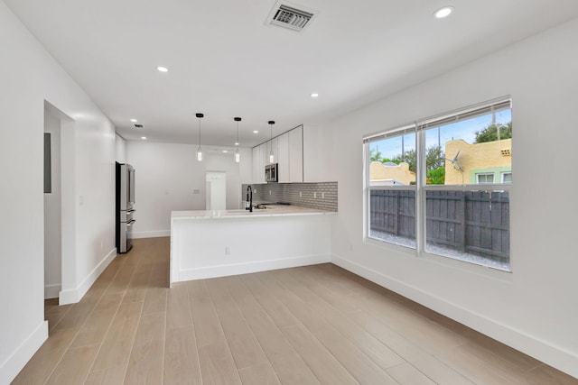 kitchen with stainless steel appliances, white cabinets, kitchen peninsula, hanging light fixtures, and light wood-type flooring