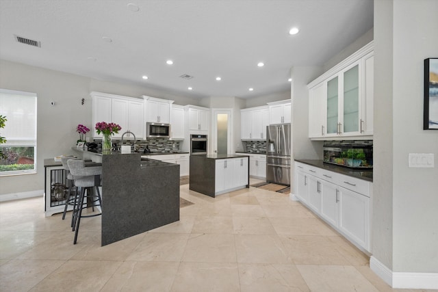 kitchen featuring white cabinets, kitchen peninsula, a breakfast bar area, backsplash, and appliances with stainless steel finishes