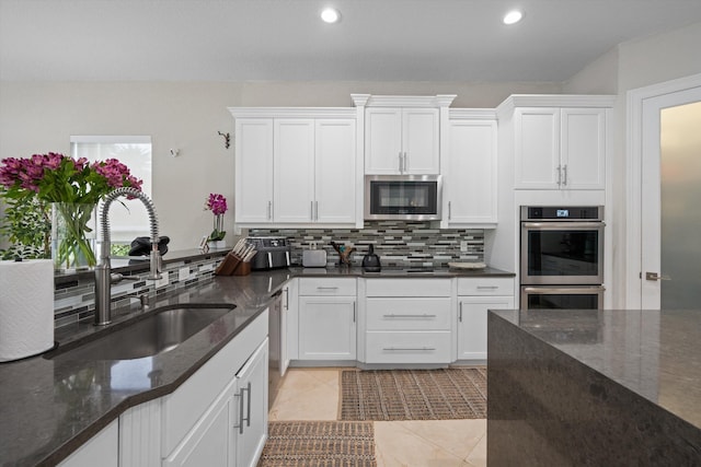 kitchen with stainless steel appliances, white cabinets, decorative backsplash, sink, and dark stone countertops