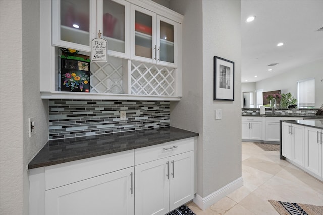 kitchen featuring dark stone counters, white cabinetry, light tile patterned floors, and backsplash