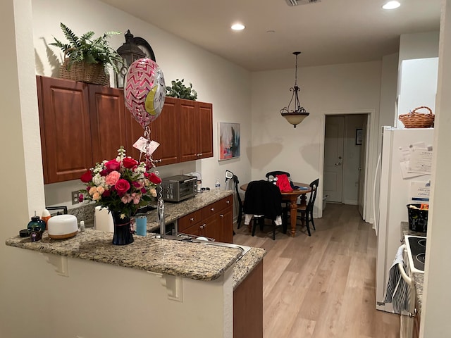 kitchen with white refrigerator, light stone countertops, hanging light fixtures, light hardwood / wood-style floors, and kitchen peninsula