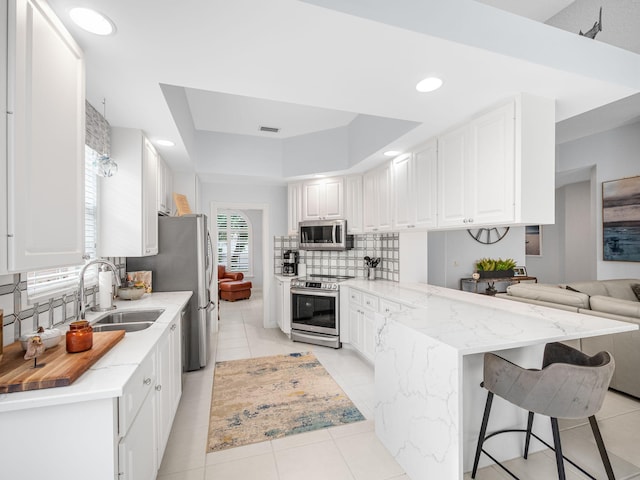 kitchen with stainless steel appliances, kitchen peninsula, sink, tasteful backsplash, and white cabinetry