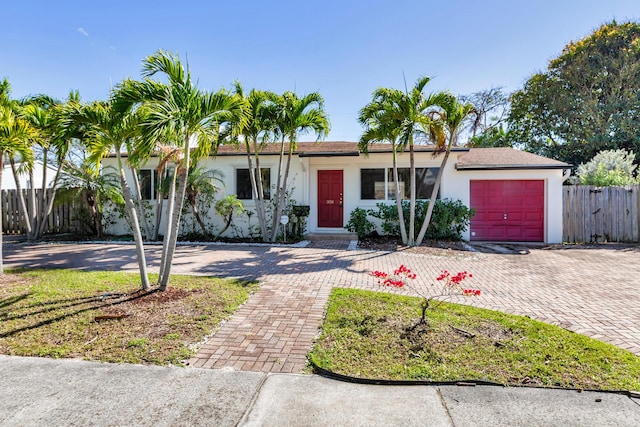 ranch-style house with an attached garage, fence, decorative driveway, and stucco siding