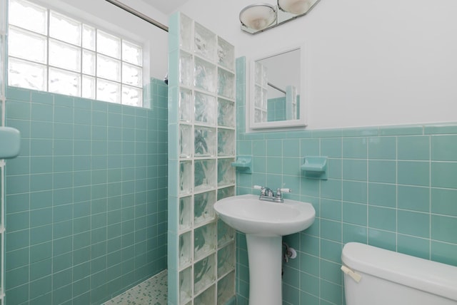 bathroom featuring toilet, wainscoting, walk in shower, and tile walls