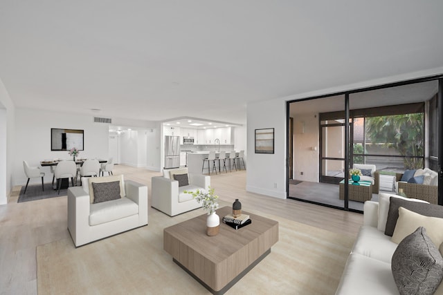 living area featuring light wood-style flooring, floor to ceiling windows, visible vents, and baseboards