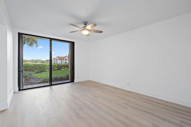 spare room featuring expansive windows, baseboards, ceiling fan, and light wood finished floors