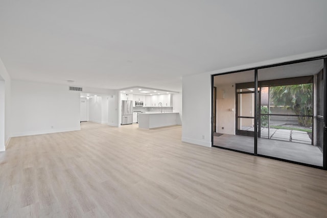 unfurnished living room with floor to ceiling windows, light wood finished floors, visible vents, a sink, and baseboards