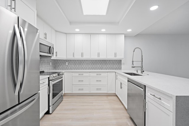 kitchen featuring light wood-style flooring, a peninsula, a sink, appliances with stainless steel finishes, and a raised ceiling