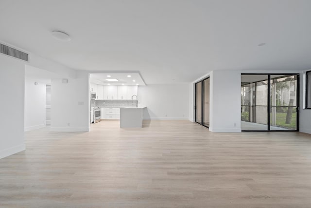 unfurnished living room featuring baseboards, visible vents, light wood-style floors, a sink, and recessed lighting