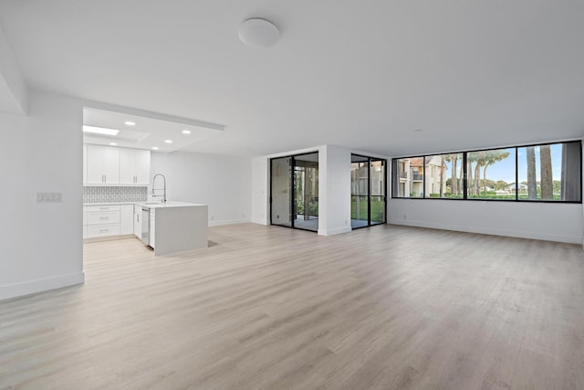 unfurnished living room with light wood-type flooring, a sink, baseboards, and recessed lighting