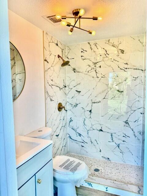 bathroom featuring toilet, vanity, a textured ceiling, and a tile shower