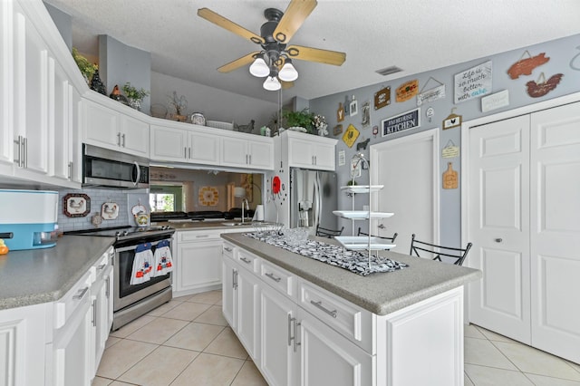 kitchen featuring appliances with stainless steel finishes, white cabinetry, an island with sink, backsplash, and light tile patterned floors