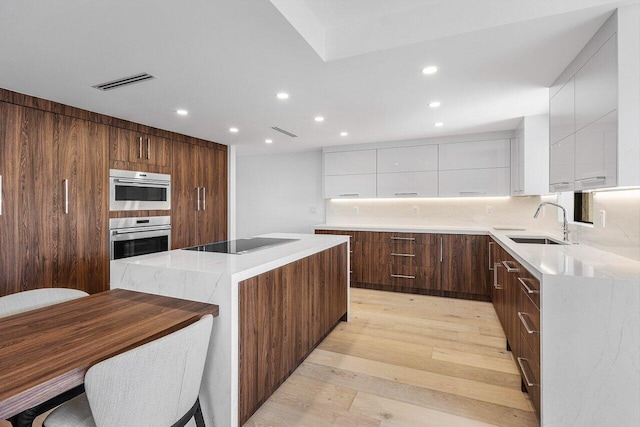 kitchen featuring white cabinets, black electric stovetop, light hardwood / wood-style floors, a kitchen island, and stainless steel double oven