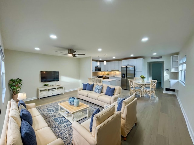 living room with light hardwood / wood-style floors, ceiling fan, and sink