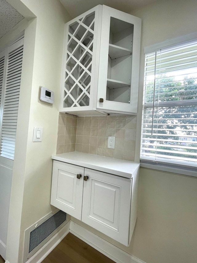 bar featuring dark hardwood / wood-style flooring, tasteful backsplash, white cabinetry, and a healthy amount of sunlight