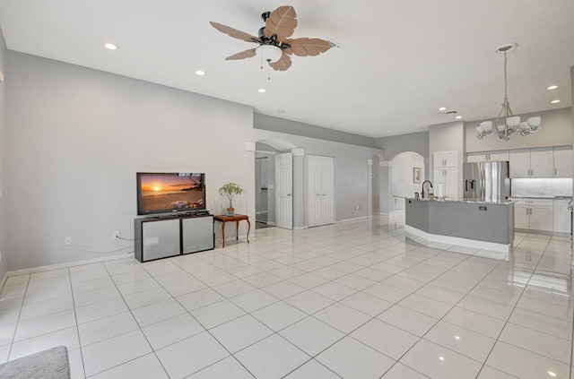 unfurnished living room with sink, ceiling fan with notable chandelier, and light tile patterned flooring