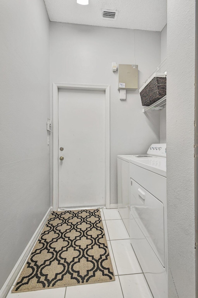 laundry area featuring light tile patterned floors, a textured ceiling, and washer and clothes dryer